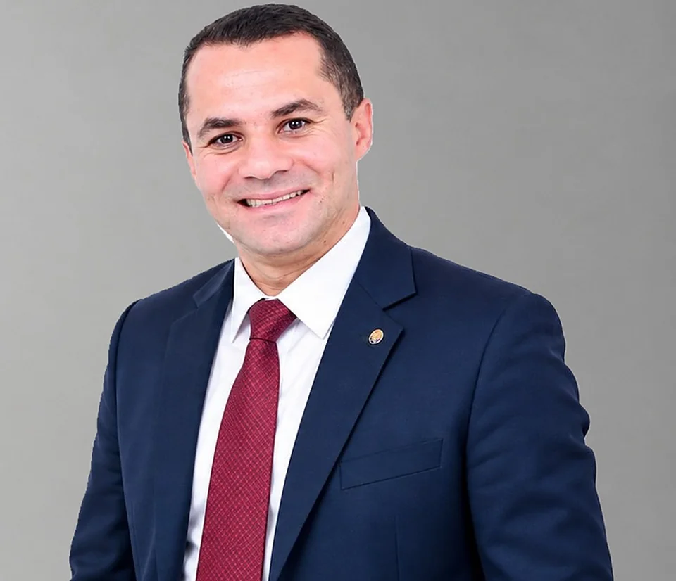 Adriano Arestides sorrindo, de terno azul-marinho e gravata bordô